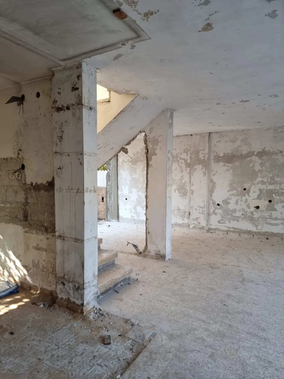 חלל מרכזי בשלד בטון חשוף עם עמודים ומדרגות בזמן השיפוץ