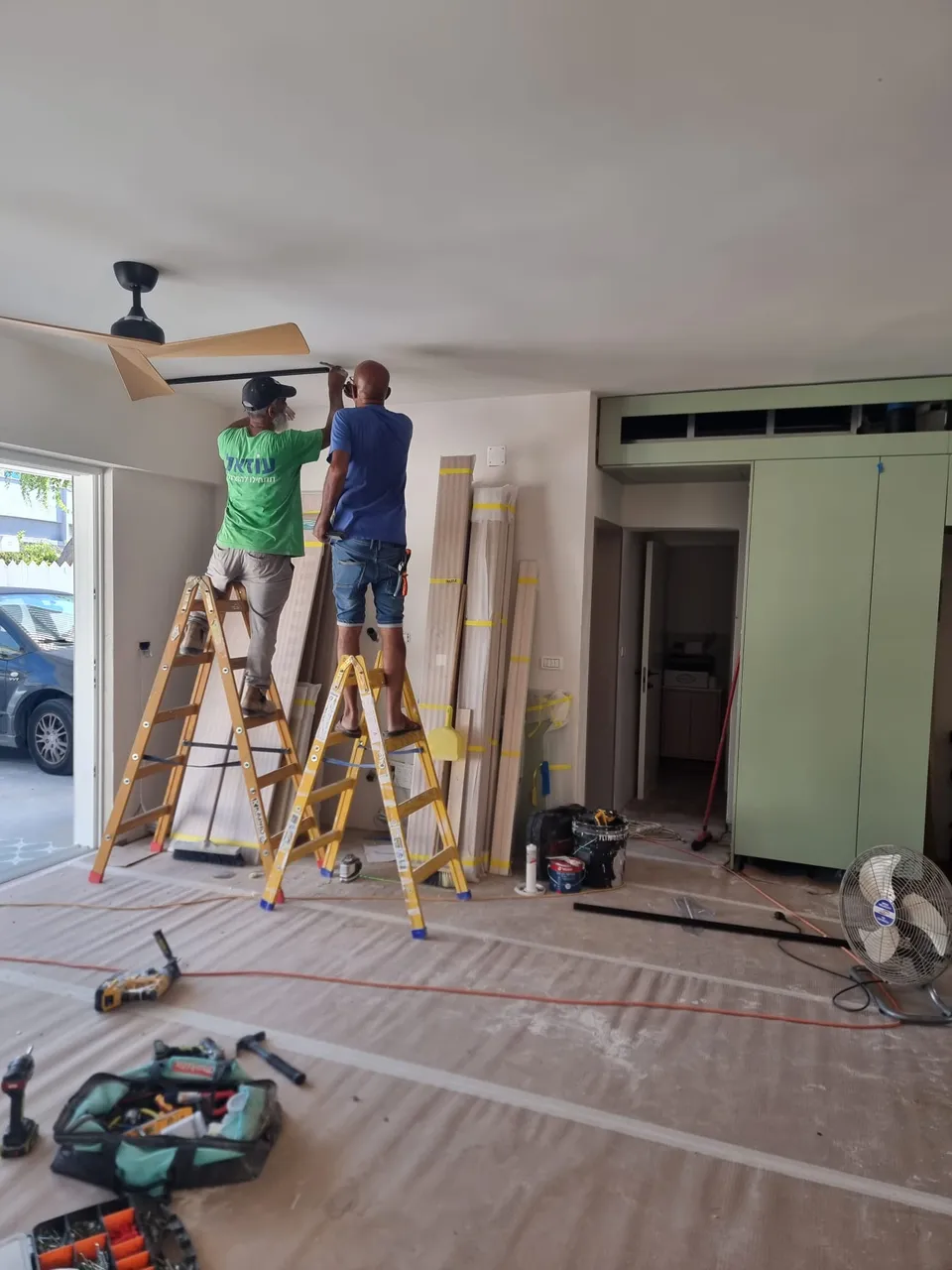 שני נגרים מתקינים מאוורר תקרה וגוף תאורה בסלון
