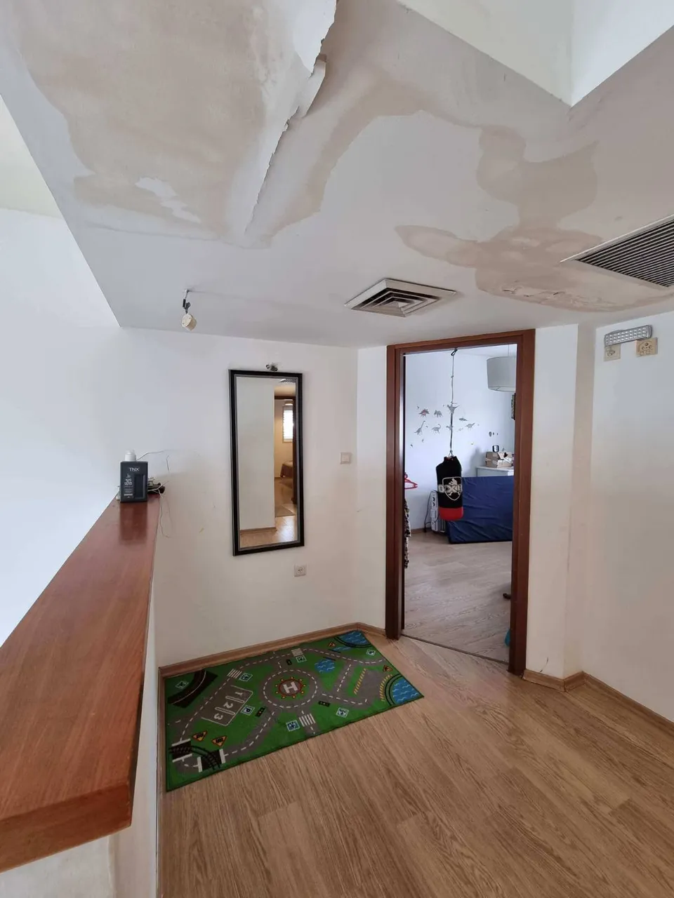 מסדרון כניסה ישן עם כתמי רטיבות בתקרה ושטיח משחק לילדים